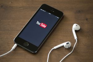 Kiev, Ukraine - June 5, 2014: Brand new Apple iPhone 5S with YouTube application service on the screen lying on a desk with headphones. YouTube is the world's most popular online video-sharing website that founded in February 14, 2005