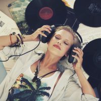 A young woman listening to music while lying on her back and surrounded by records