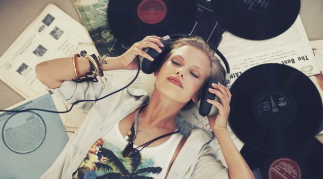 A young woman listening to music while lying on her back and surrounded by records